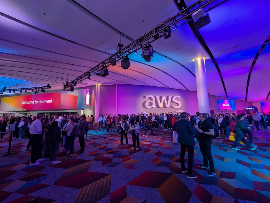 Menschenmenge in einem modernen Veranstaltungsraum mit AWS-Logo und buntem Licht.