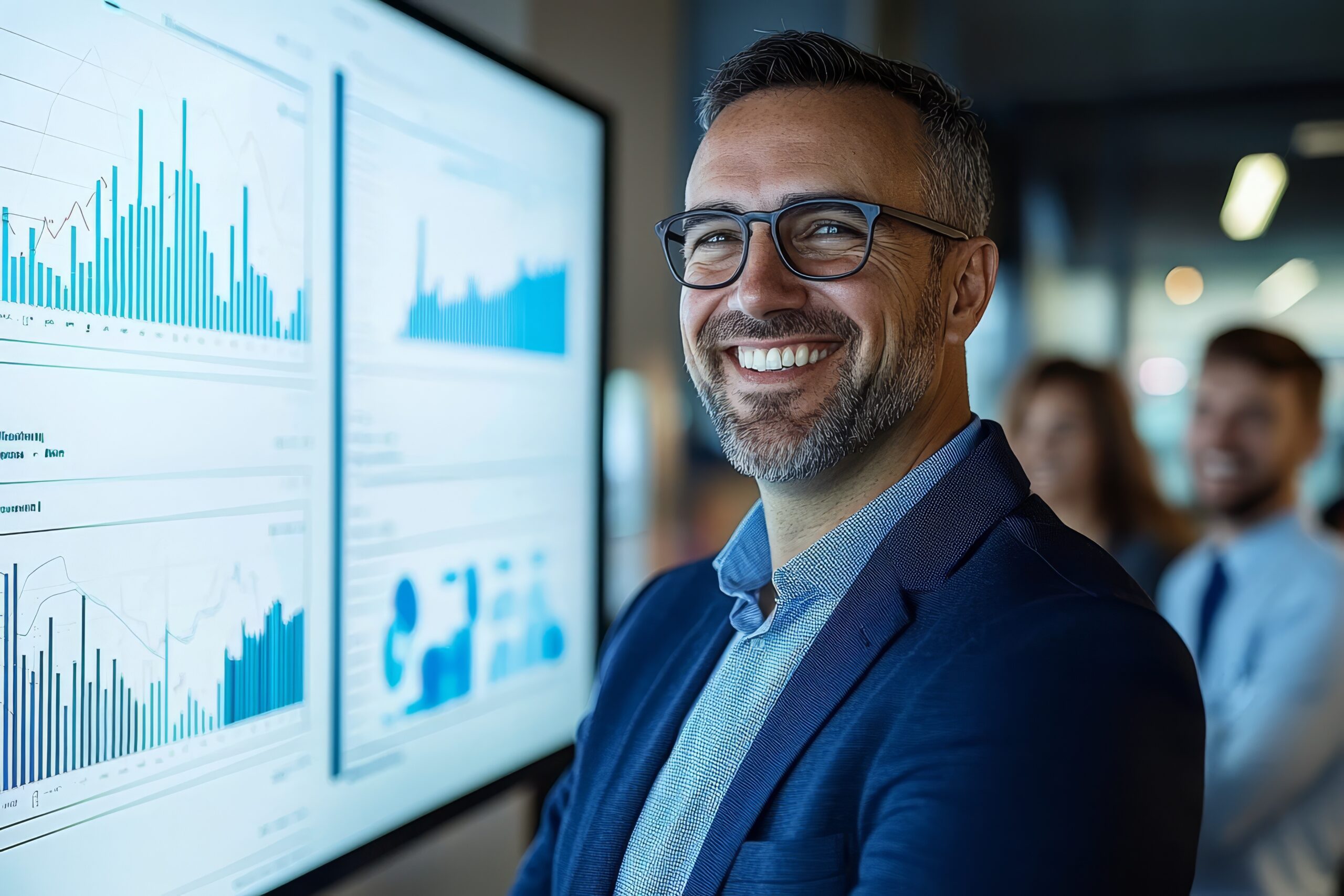 Mann mit Brille und Anzug l&auml;chelt vor einem Bildschirm mit Datenanalysen und Diagrammen.
