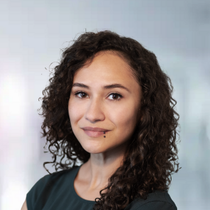 Porträt einer Frau mit lockigem Haar und einem Lippenpiercing, neutraler Hintergrund.