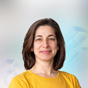 Eine junge Frau mit braunen Haaren, die ein gelbes T-Shirt trägt, lächelt vor einem verschwommenen, hellen Hintergrund.